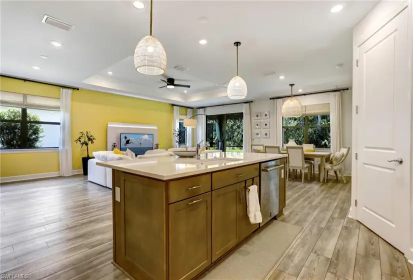 Kitchen featuring light hardwood / wood-style floors, stainless steel dishwasher, an island with sink, decorative light fixtures, and a raised ceiling