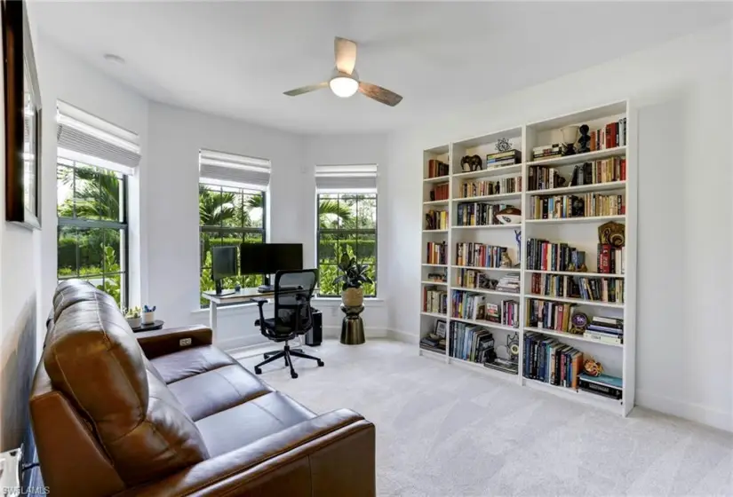 Carpeted office space with ceiling fan and built in shelves