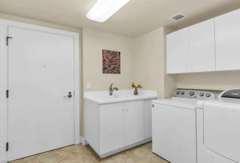 Laundry room with sink, washing machine and dryer, light tile flooring, and cabinets